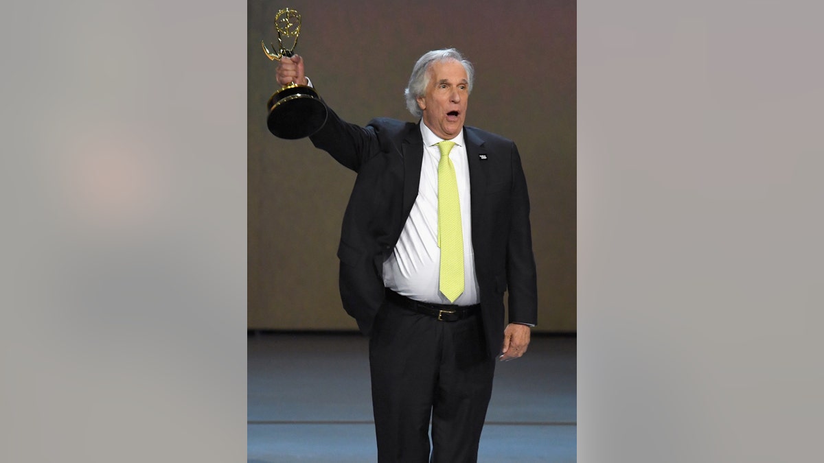 Henry Winkler in a suit and neon yellow tie accepting an Emmy Award