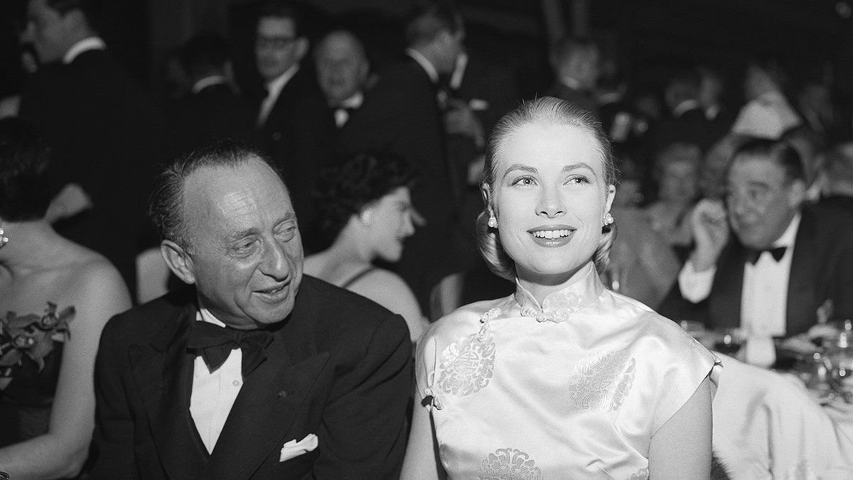 Joe Pasternak in a tux looking at Grace Kelly in a satin white gown