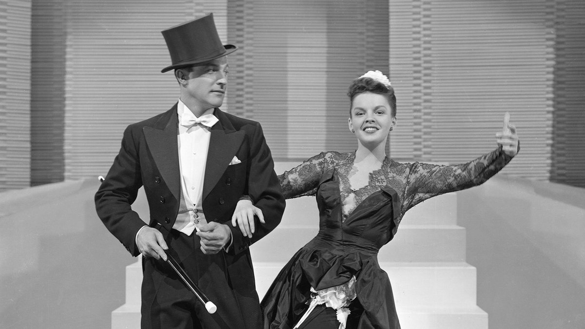 Gene Kelly in a top hat and tails dancing with Judy Garland in a glamorous gown
