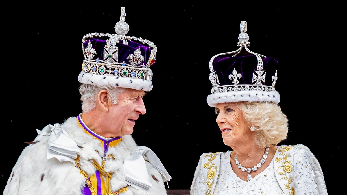 A close-up of King Charles and Queen Camilla looking at each other as they wear their robes and crowns