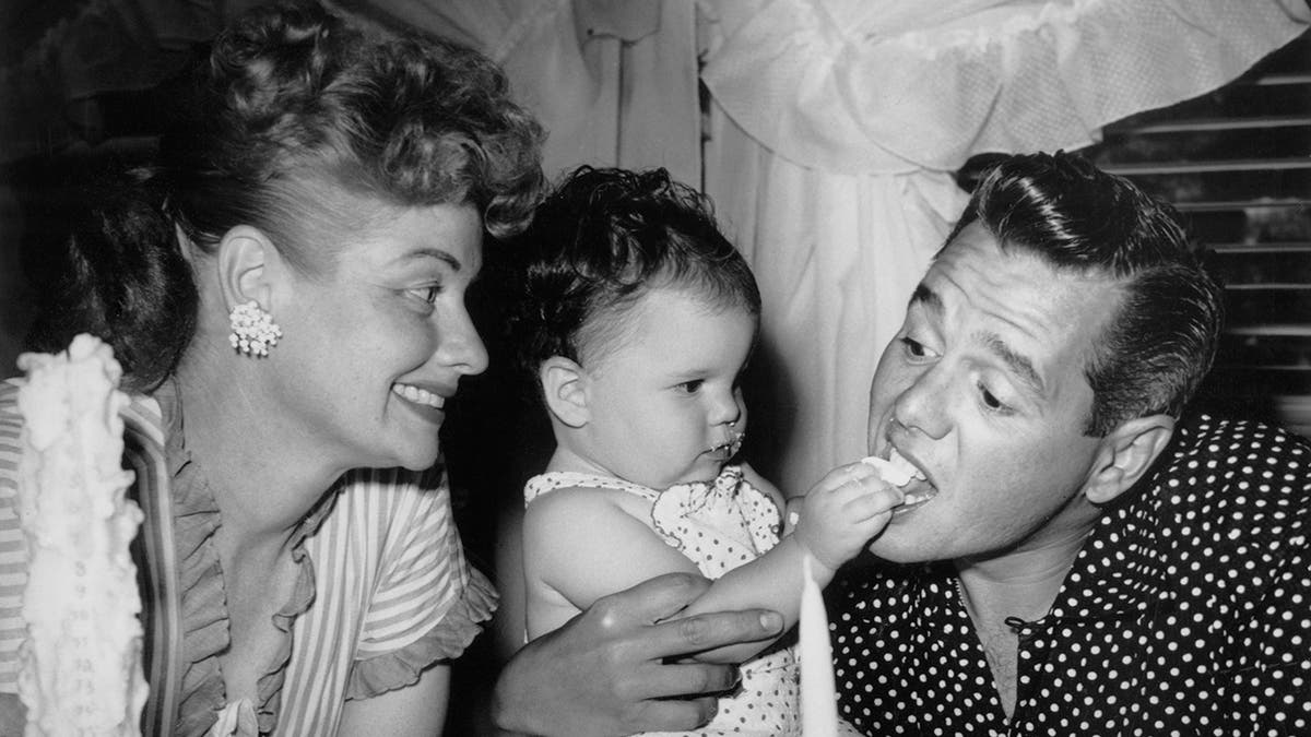 Lucille Ball smiling as her daughter Lucie Arnaz feeds her father Desi Arnaz a piece of cake