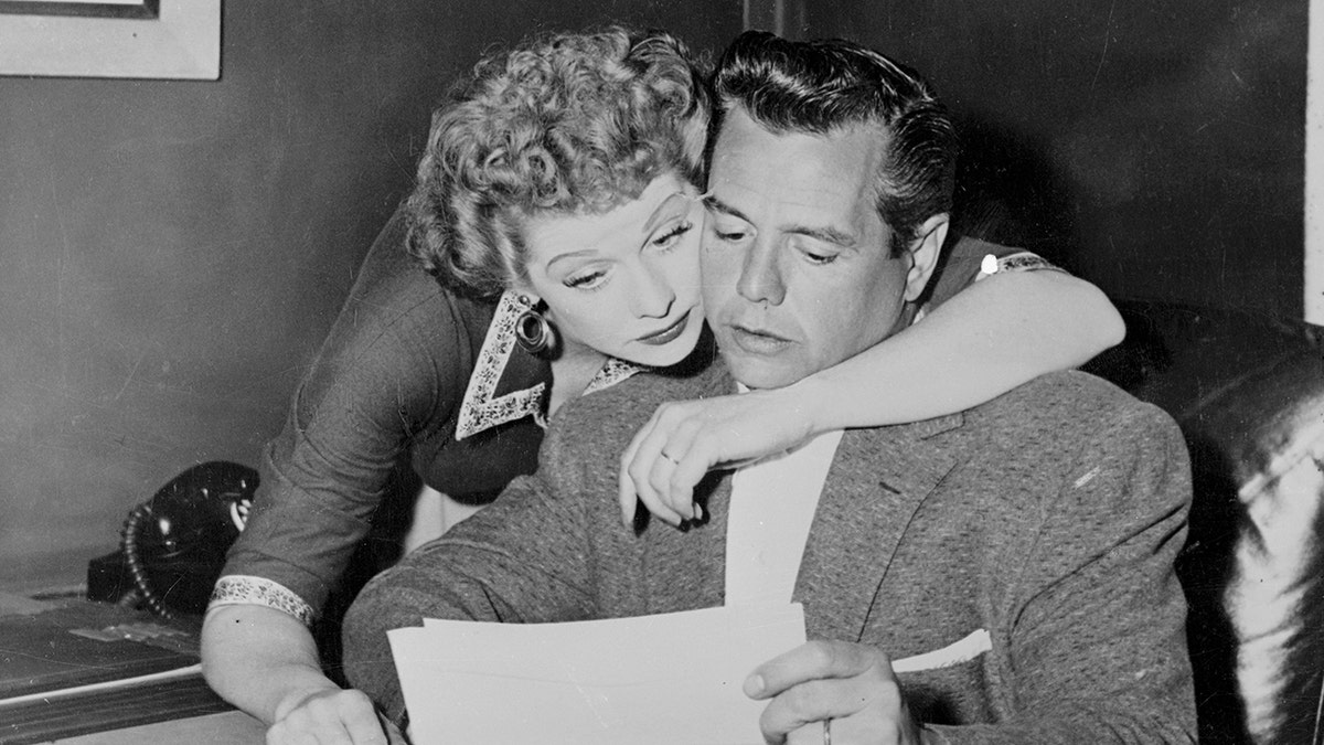 Lucille Ball embracing Desi Arnaz from behind as he reads a letter