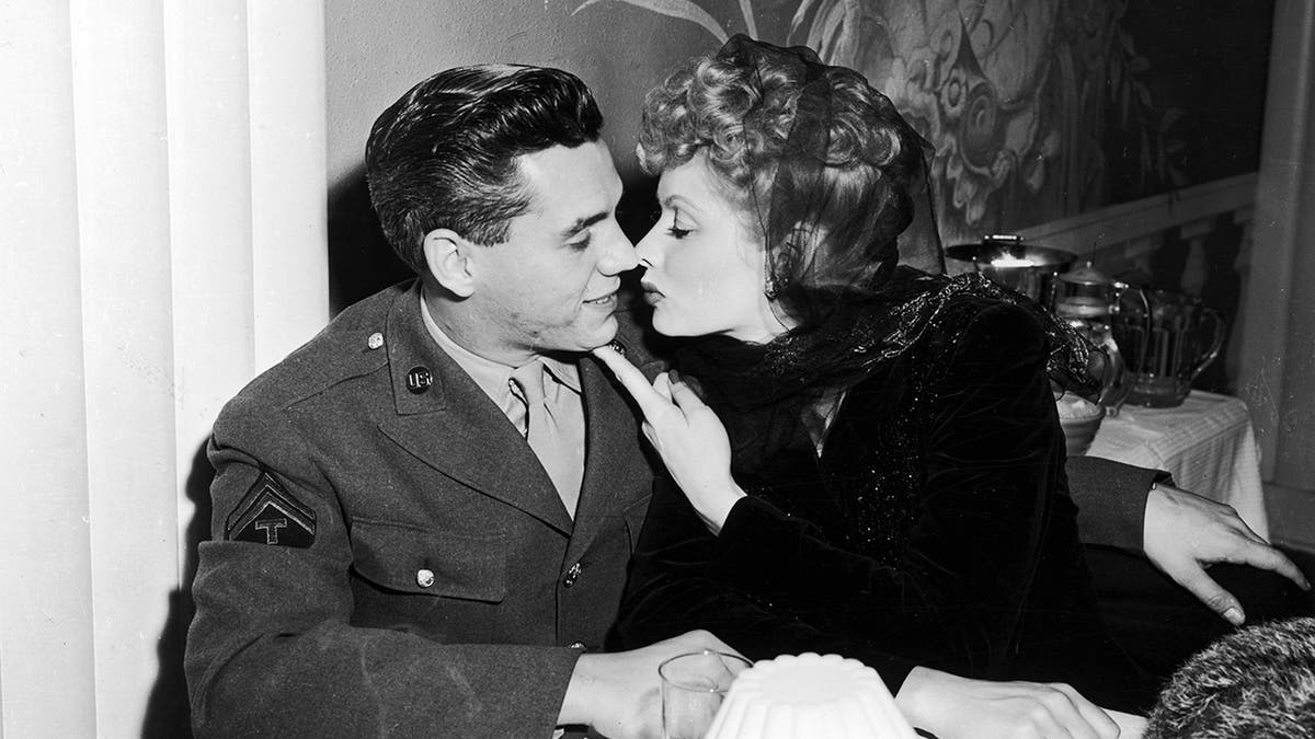 Lucille Ball wearing a black dress leaning in for a kiss from Desi Arnaz in a military suit