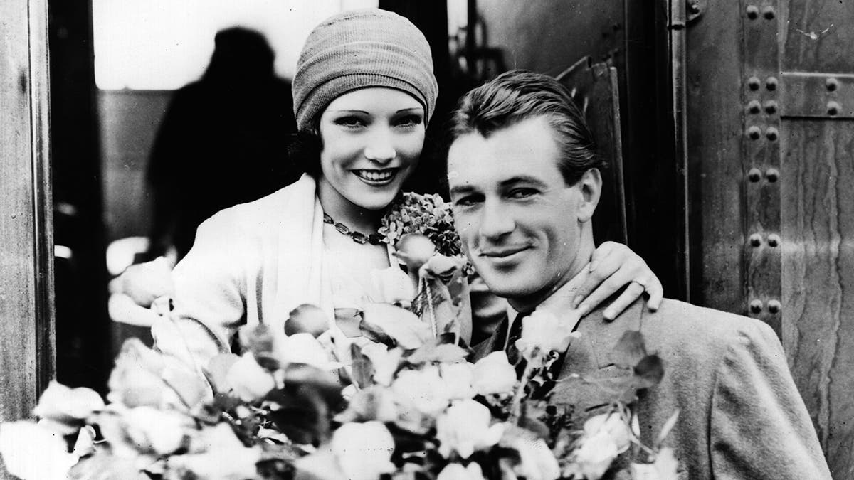 Lupe Velez having her arms around Gary Cooper who is holding a bouquet of flowers