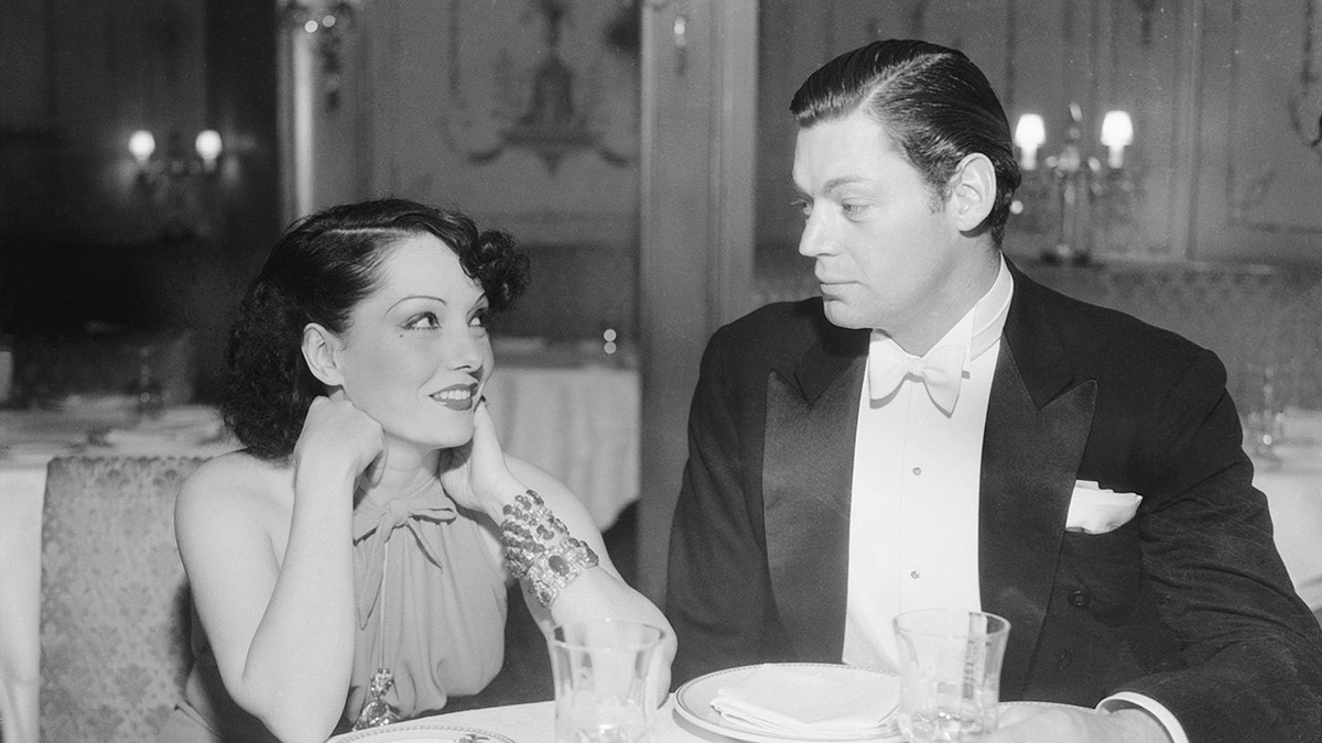 Lupe Velez looking adoringly at Johnny Weissmuller as they both wear formal wear at dinner