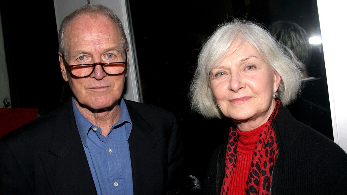 Paul Newman wearing a blue shirt and a black blazer next to Joanne Woodwasrd in a red blouse and matching black blazer