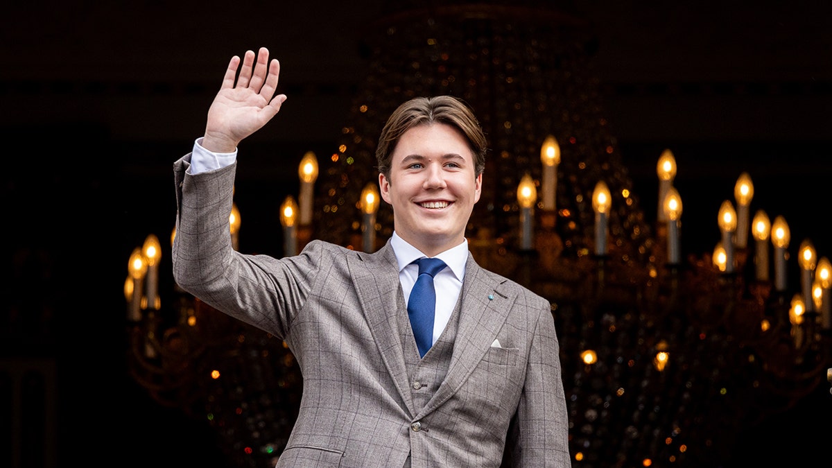 Prince Christian of Denmark wearing a gray suit and waving to a crowd