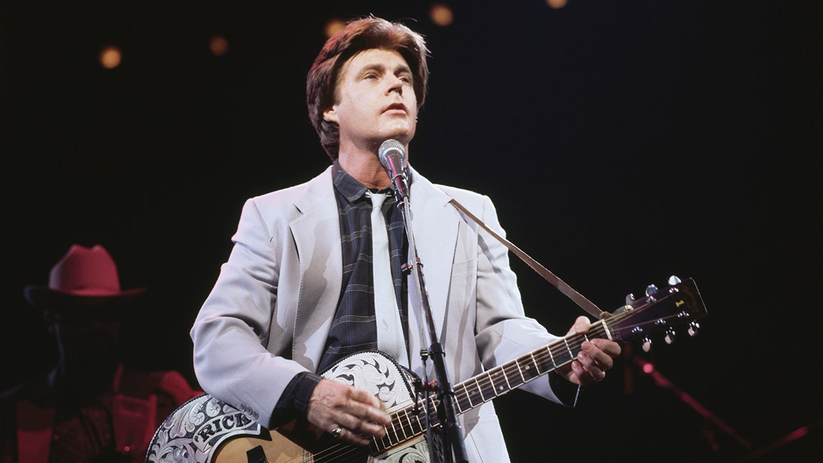 Ricky Nelson wearing a grey suit playing a guitar