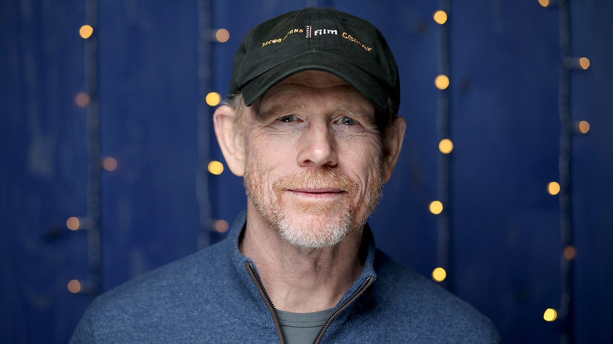 A close-up of Ron Howard wearing a blue shirt and a black cap
