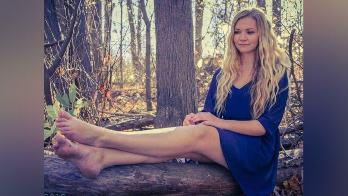 Gina wearing a blue dress and sitting on a log in the woods.