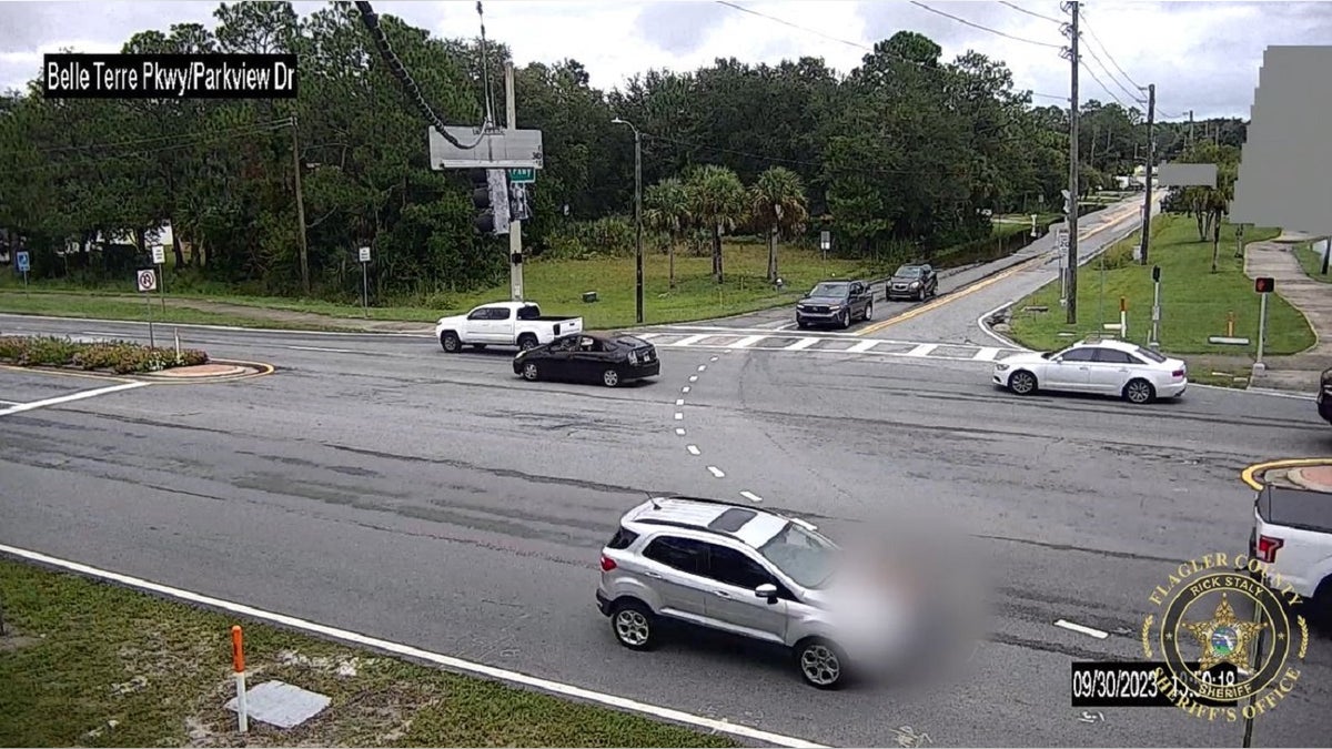 Surveillance video showing a vehicle allegedly driven by Cheryl Henderson with a blurred image of someone on top on her car hood on a busy street