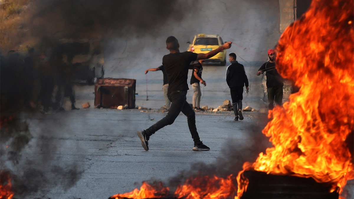 Palestinians hurling rocks on street with fire in foreground