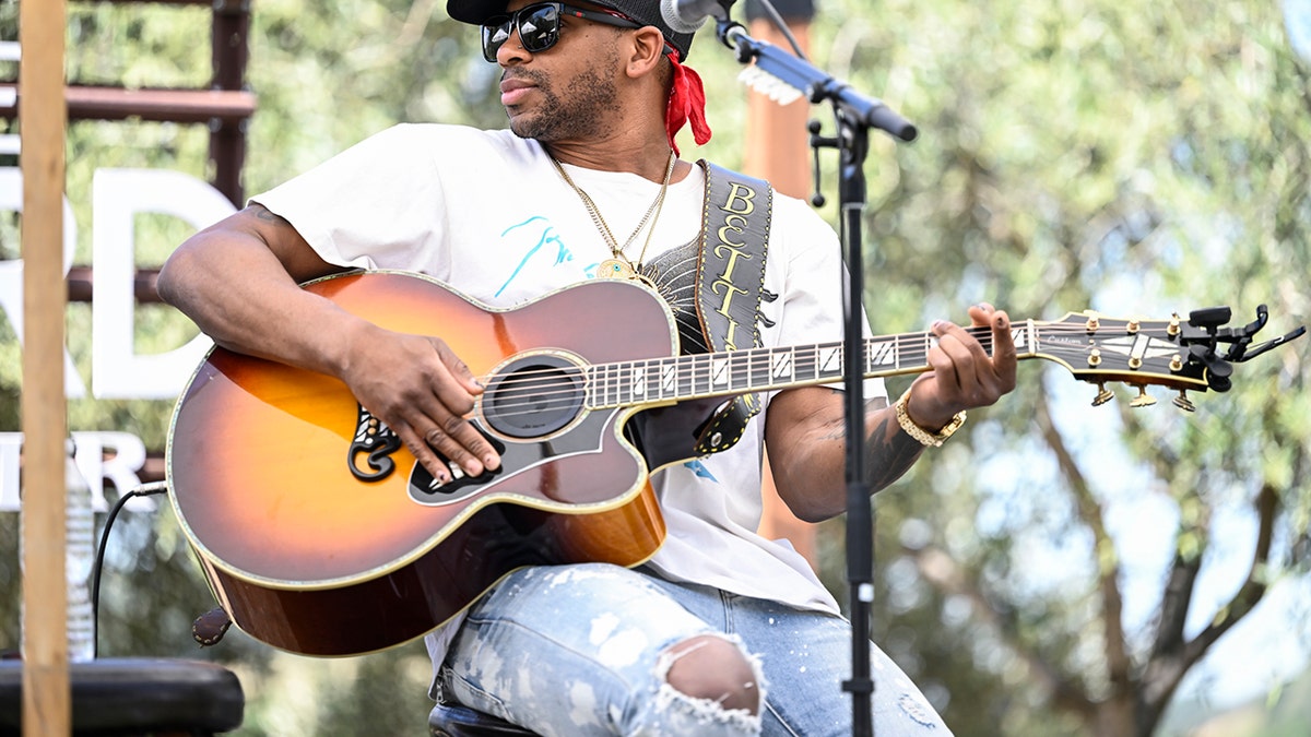 Jimmie Allen sitting on stage with guitar