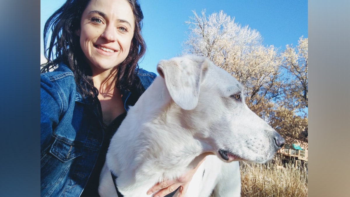 Woman smiles as she poses with white dog.