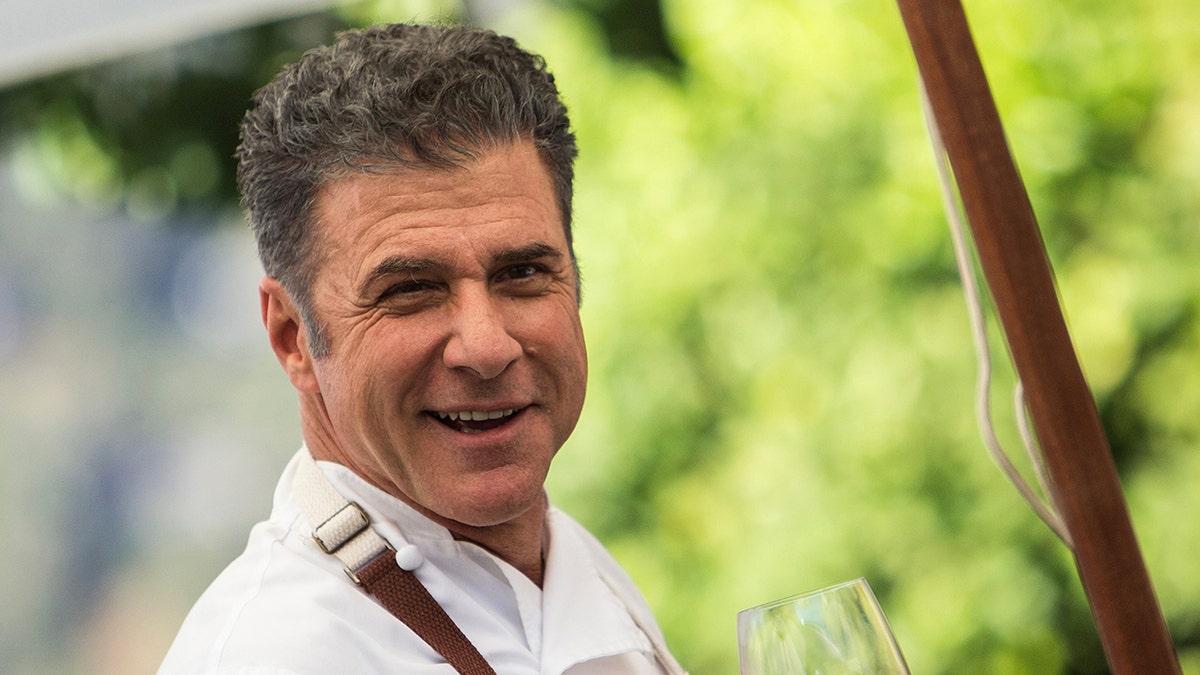 Michael Chiarello sorride con in mano un bicchiere di vino in una vigna