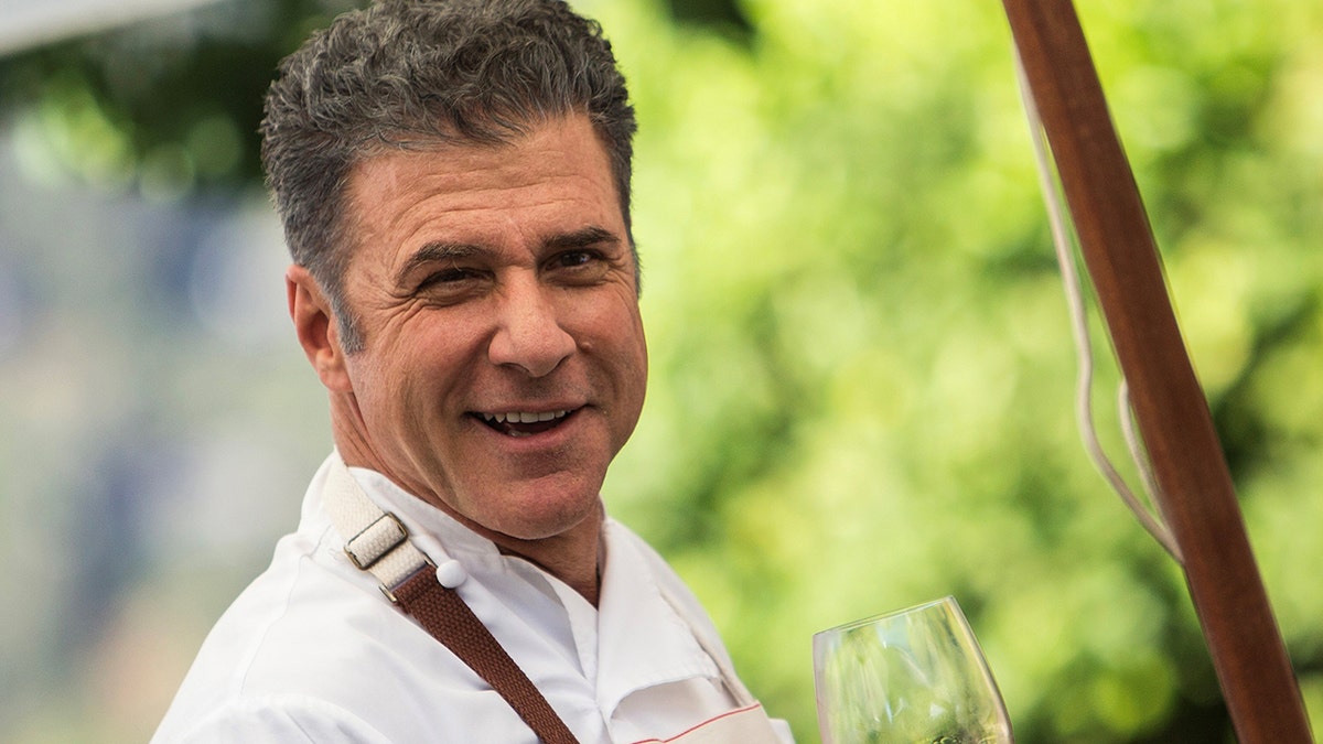 Michael Chiarello sorride con in mano un bicchiere di vino in una vigna