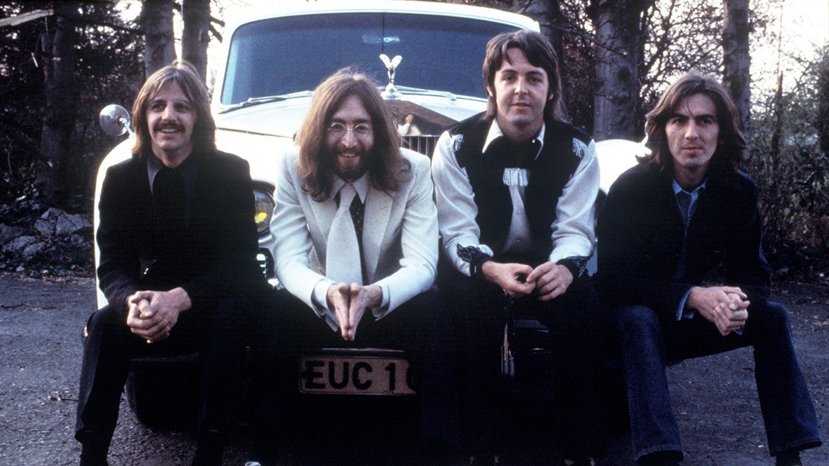 The Beatles posing together on the bumper of a car