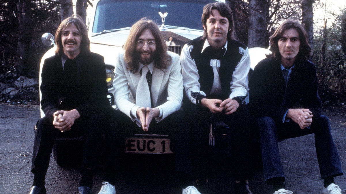 The Beatles posing together on the bumper of a car