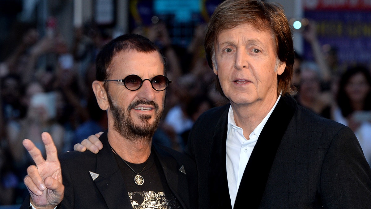 Ringo Starr flashing a peace sign while posing with Paul McCartney