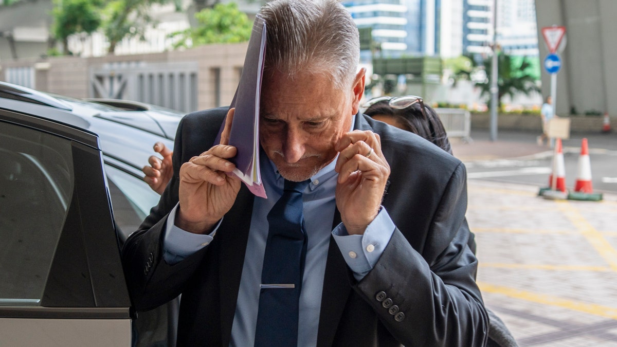 Sen. Jeff Wilson covers his face as he arrives at court in Hong Kong
