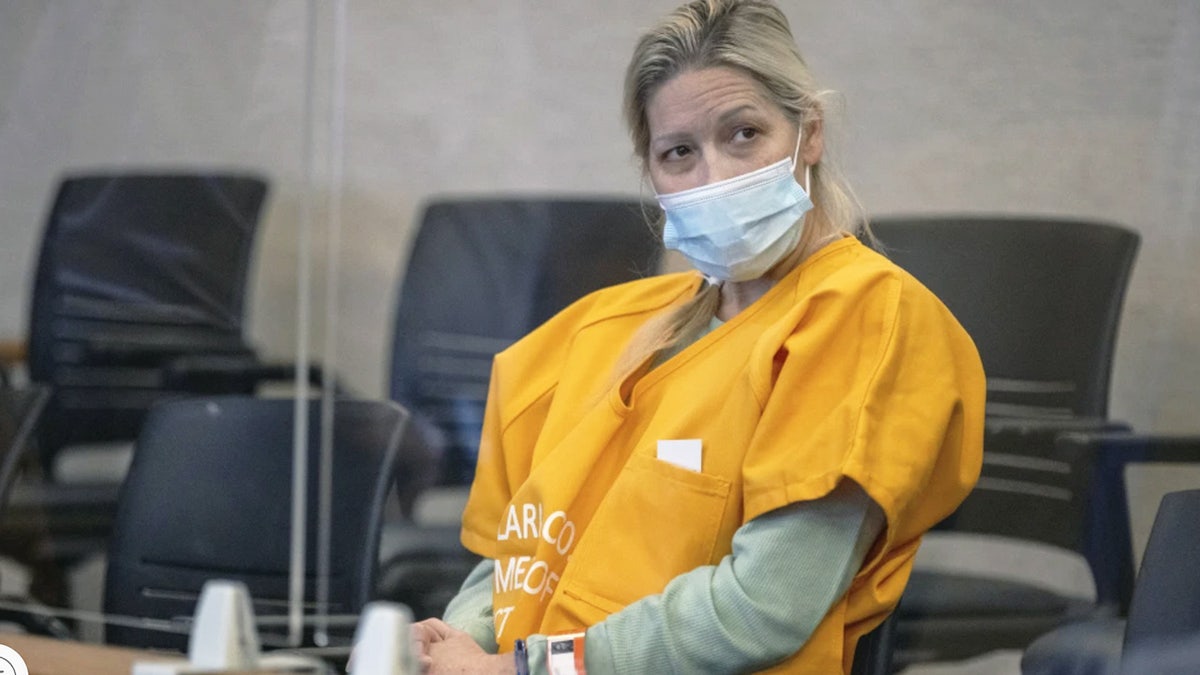 woman sits at defense table in yellow jail-issue jumpsuit.