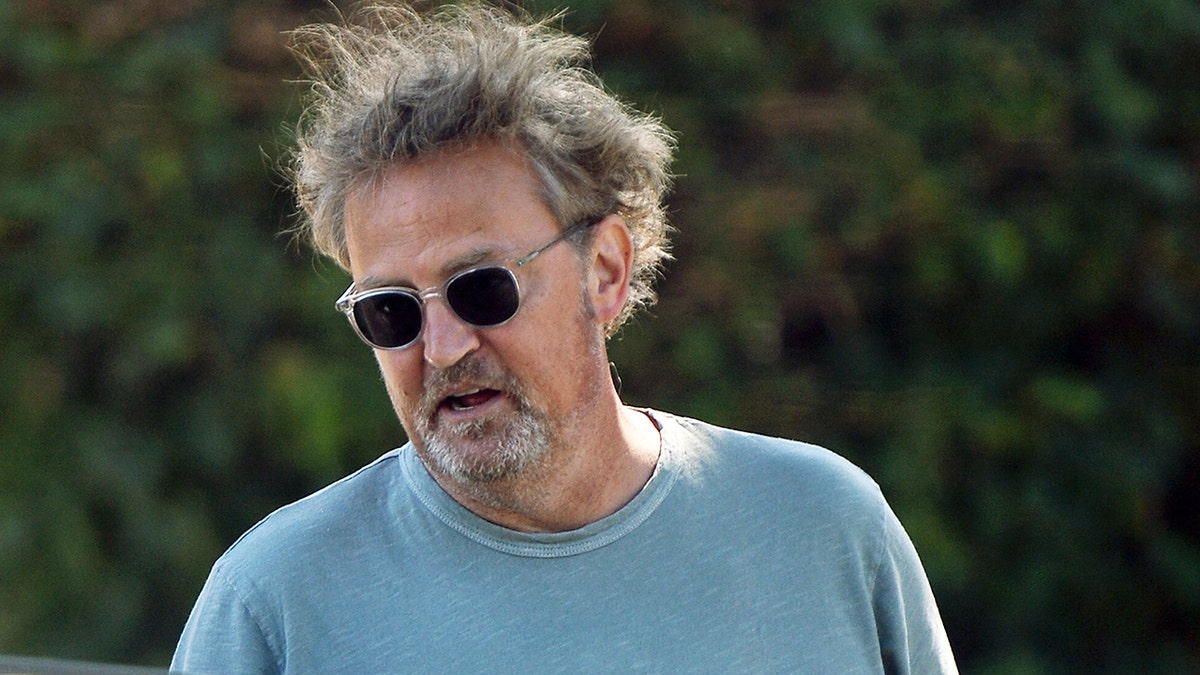 A close-up of Matthew Perry wearing sunglasses and a light blue shirt
