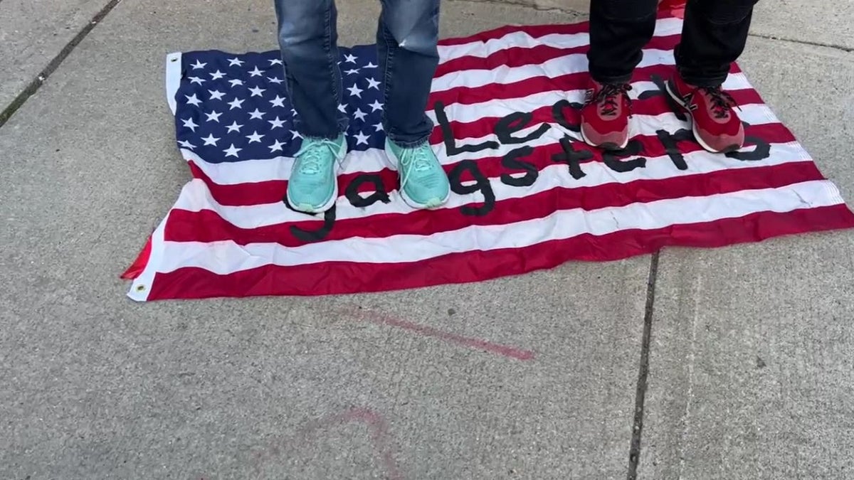 Anti-Israel protestors stand on the U.S. flag with 'Legit Gangster' written across it
