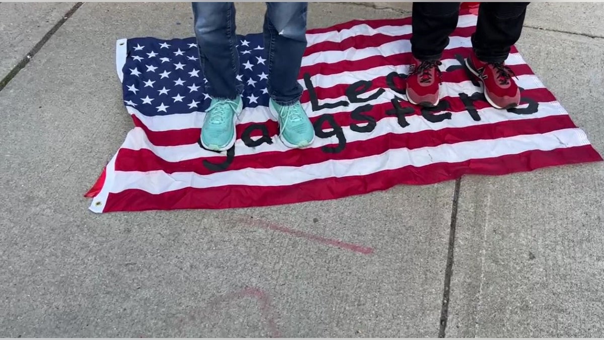 Anti-Israel protestors stand on the U.S. flag with 'Legit Gangster' written across it