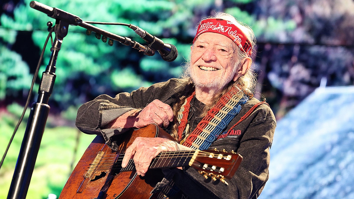 Willie Nelson smiling holding his guitar
