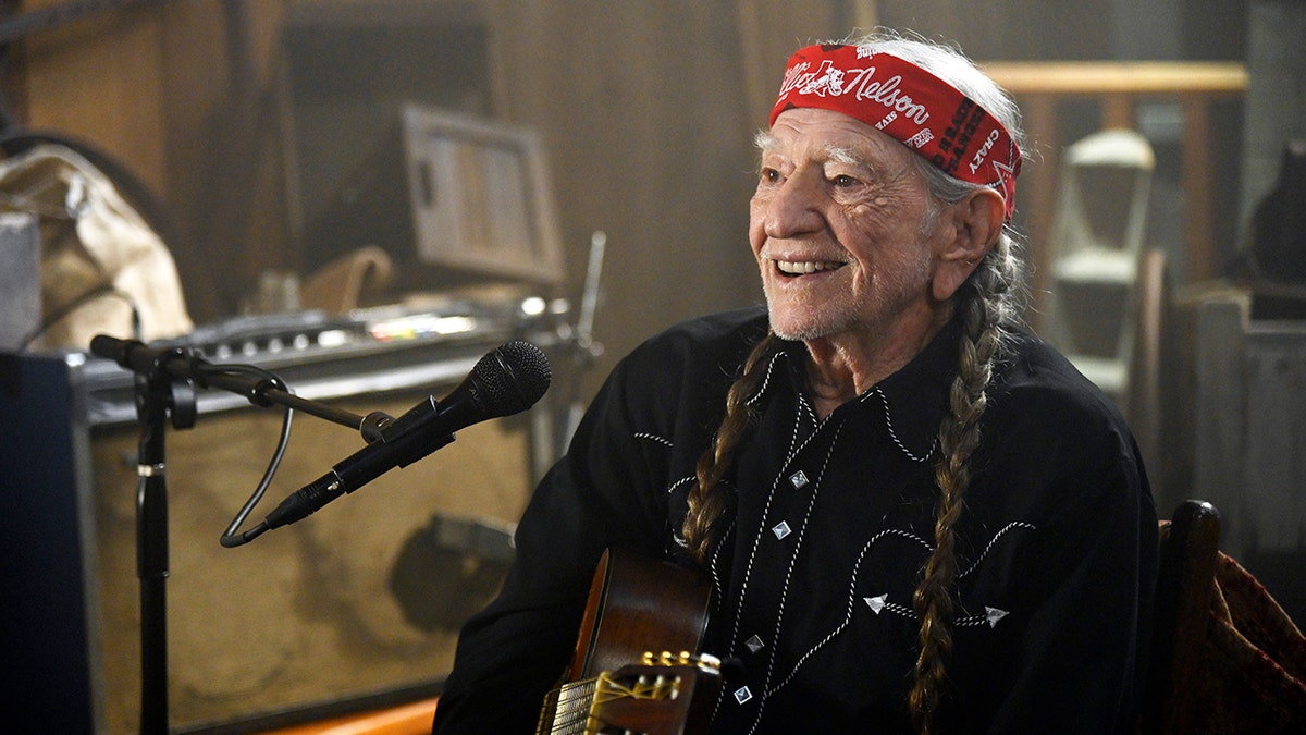 Willie Nelson sitting and smiling with guitar