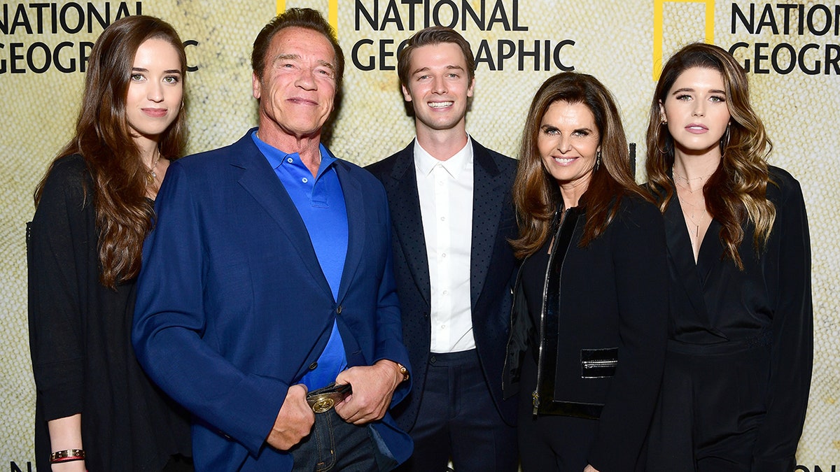 Arnold Schwarzenegger em terno e camisa azuis está ao lado de sua filha Christina (L) e filho Patrick, ex-esposa Maria Shriver e filha Katherine