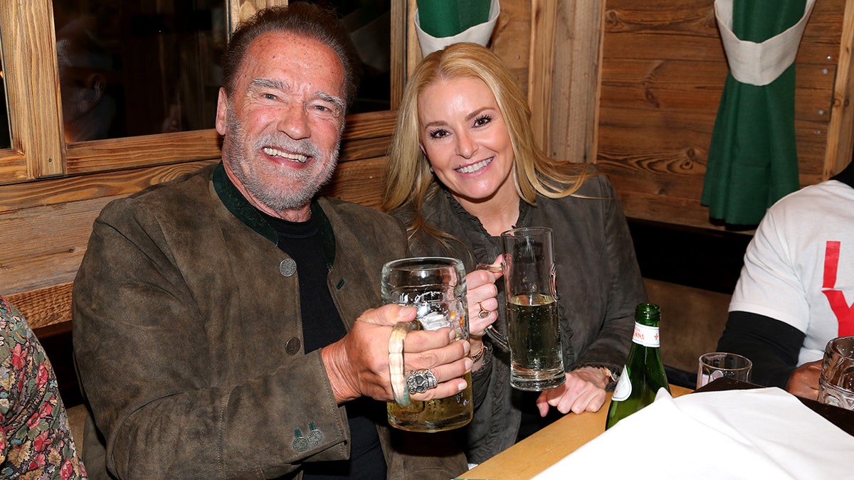 Arnold Schwarzenegger and his girlfriend Heather Milligan hold up beer cups at Oktoberfest in Munich