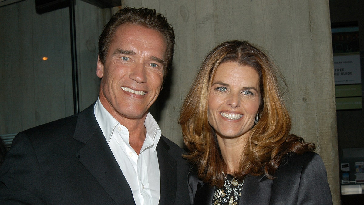 Arnold Schwarzenegger in a suit with no tie and Maria Shriver pose for a photo