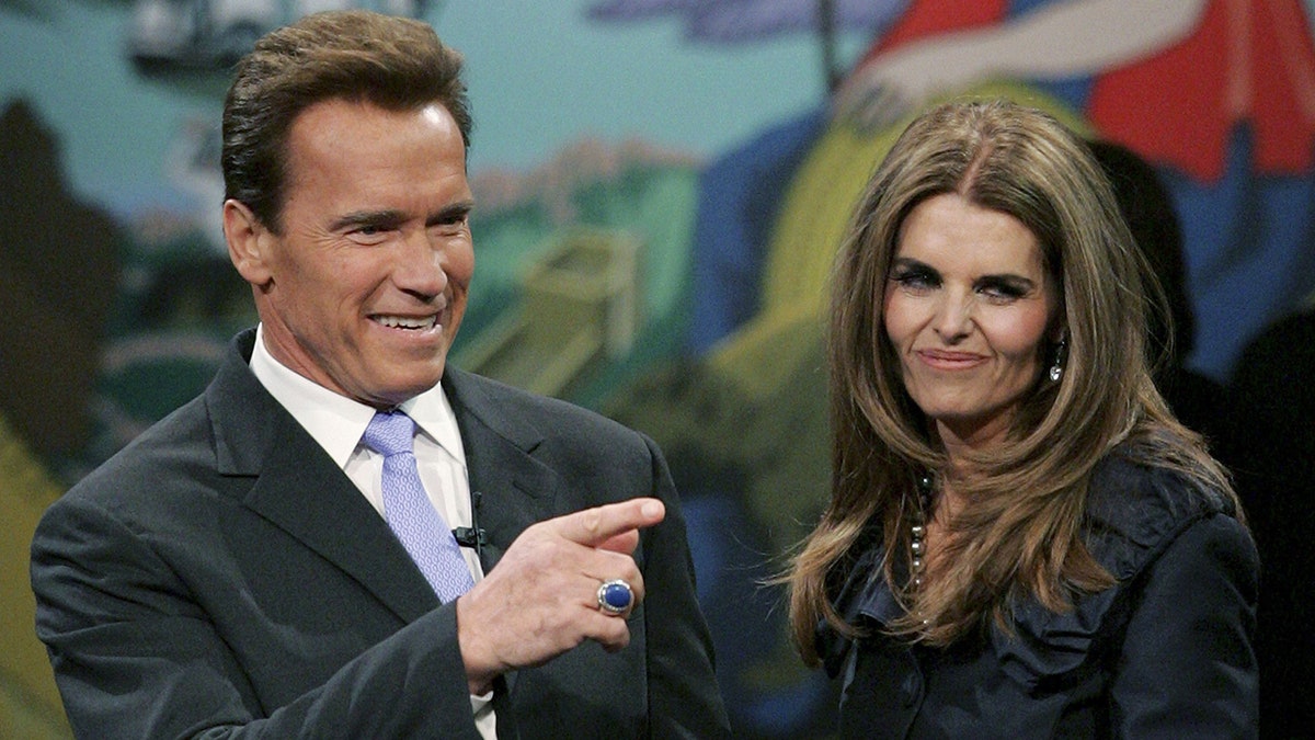 Arnold Schwarzenegger points while Maria Shriver stands next to him