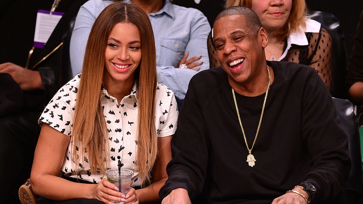 Beyonce in a white shirt sleeve button down sits courtside next to Jay-Z in a black longsleeve shirt