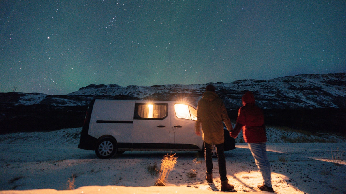 Couple standing near camper van under Aurora Borealis