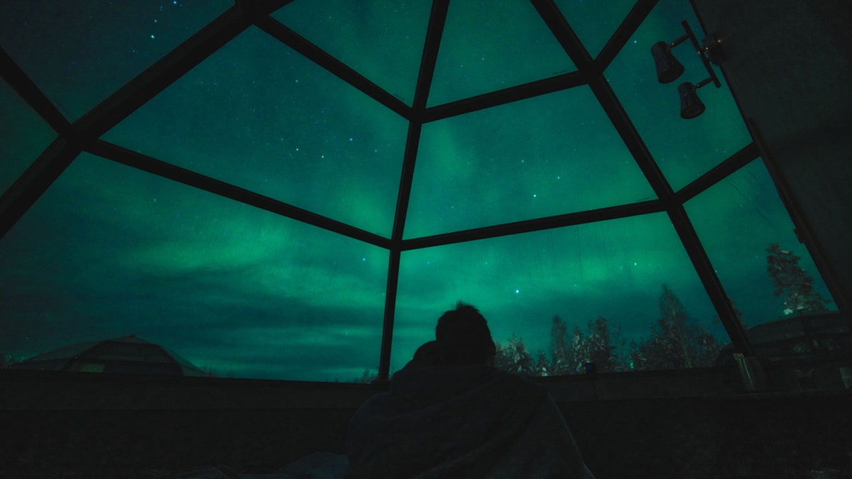 A couple enjoy view of Aurora Borealis and stars in glass igloo in Lapland, Rovaniemi, Finland