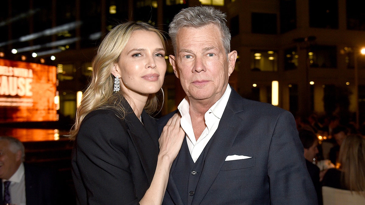 Sara Foster in a black coat puts her hand on David Foster ina black suit at an event in California