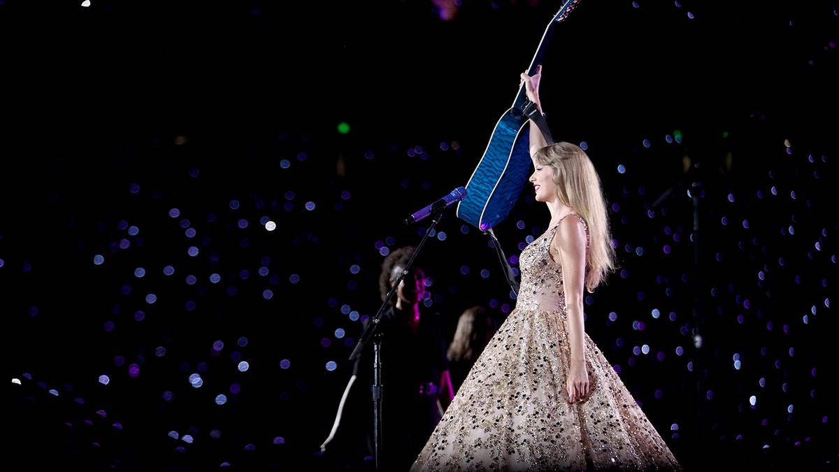 taylor swift holding up guitar on stage