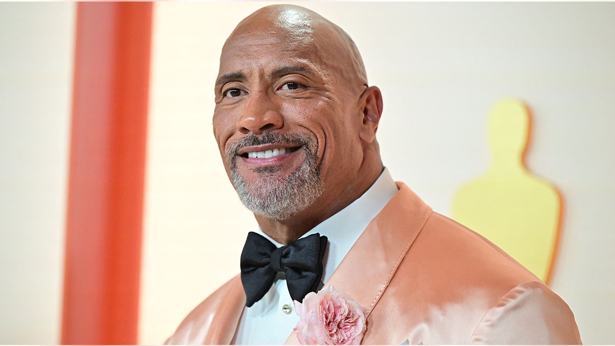 Dwayne Johnson in a peach velvet tuxedo and black bowtie on the Oscar carpet