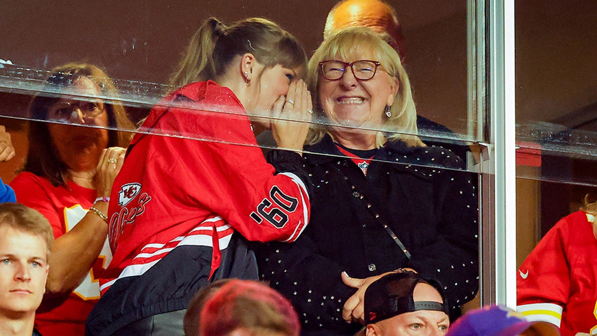 Taylor Swift in red whispers into Donna Kelce's ear who smiles while watching the Kansas City Chiefs