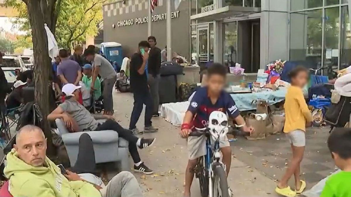 Migrants with their belongings on a crowded sidewalk right outside a Chicago police station