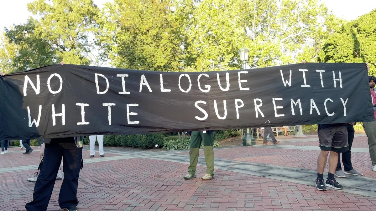 Students hold a sign reading "no dialogue with white supremacy"