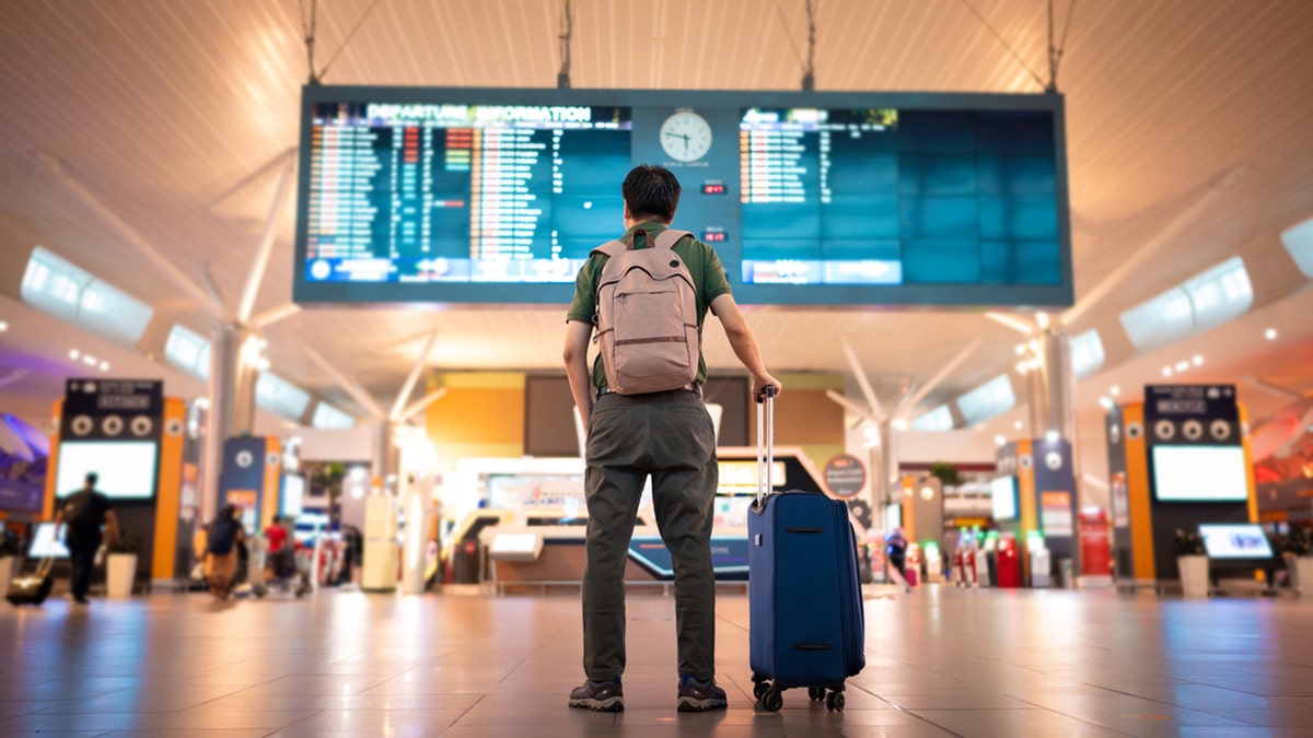 man in airport looking at arrival and departure board