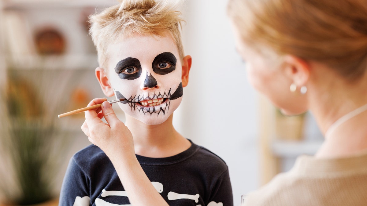 ghostface horror movie Woman paint skull face on boy wearing skeleton costume.