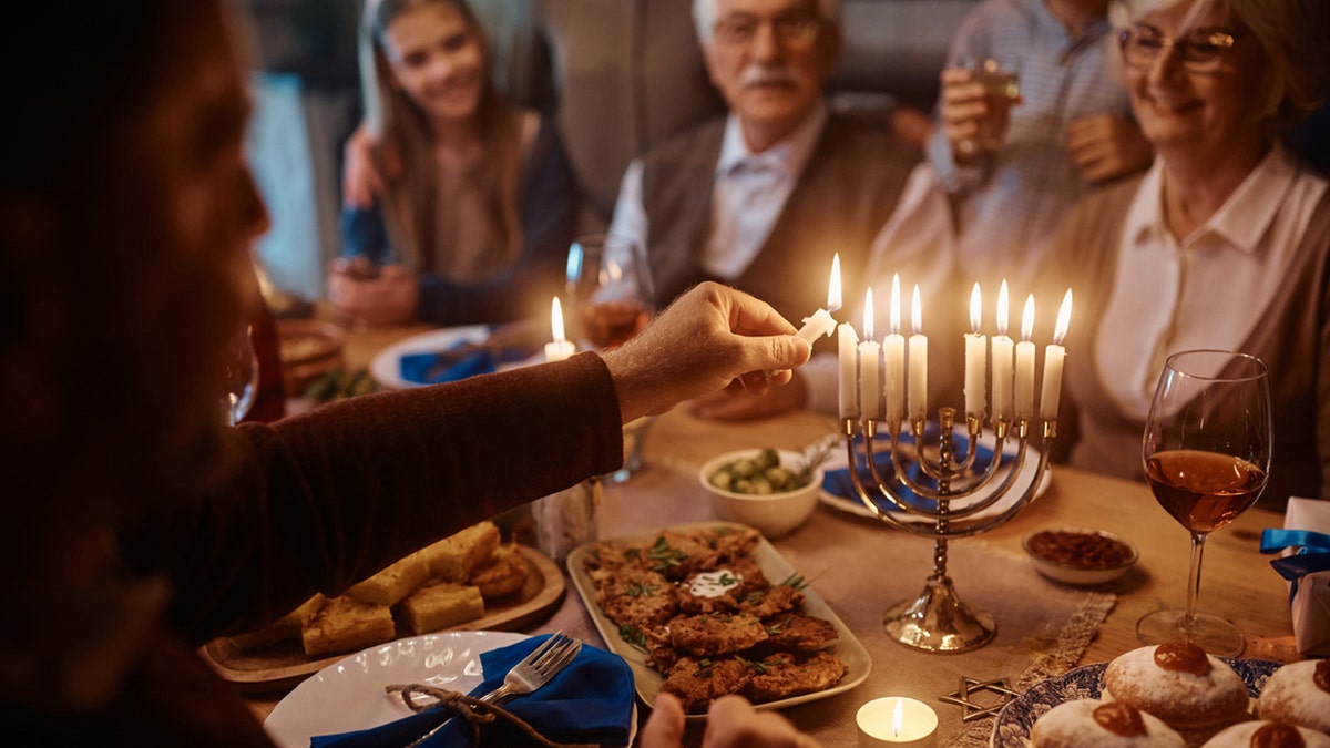 man lighting menorah with family in brackground