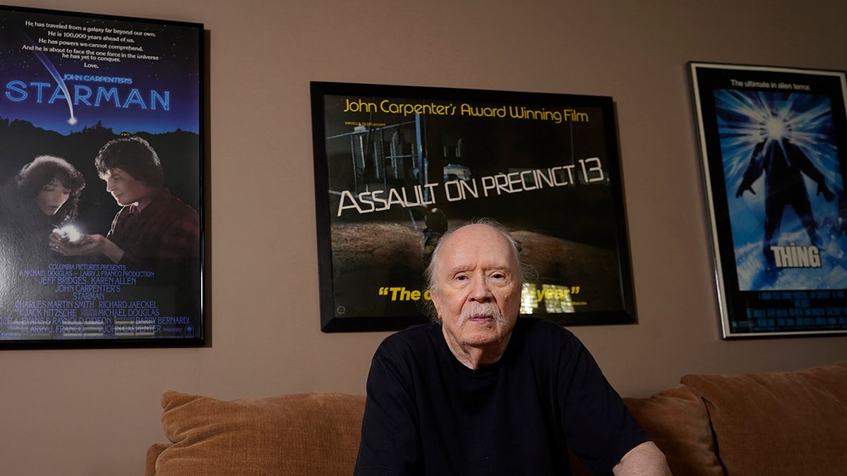 John Carpenter seduto davanti ai manifesti dei suoi film