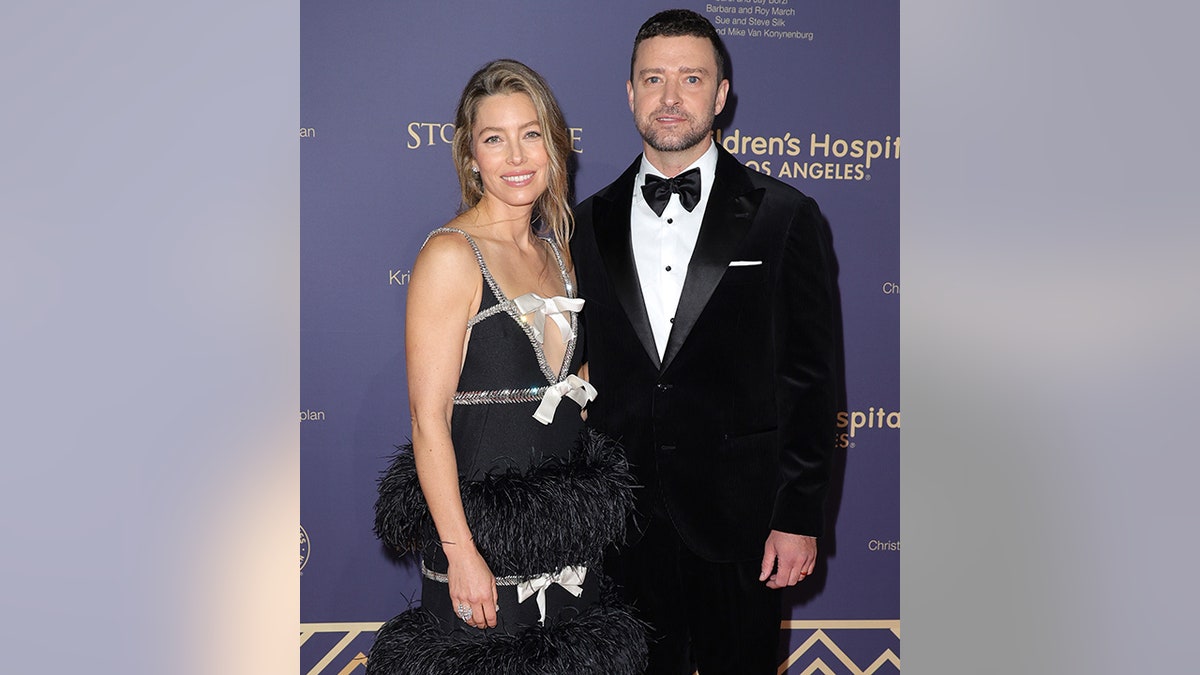 Jessica Biel in a black dress with bows smiles next to Justin Timberlake in a black tuxedo