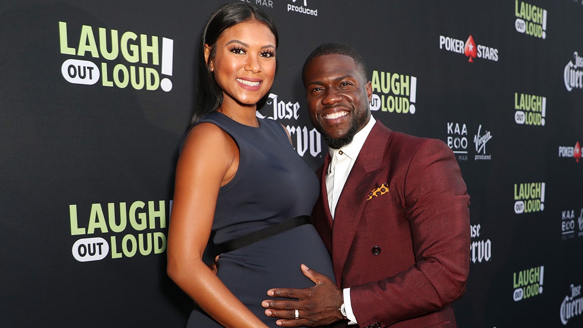 Pregnant Eniko Hart has her belly cradled by husband Kevin Hart in a dark red jacket
