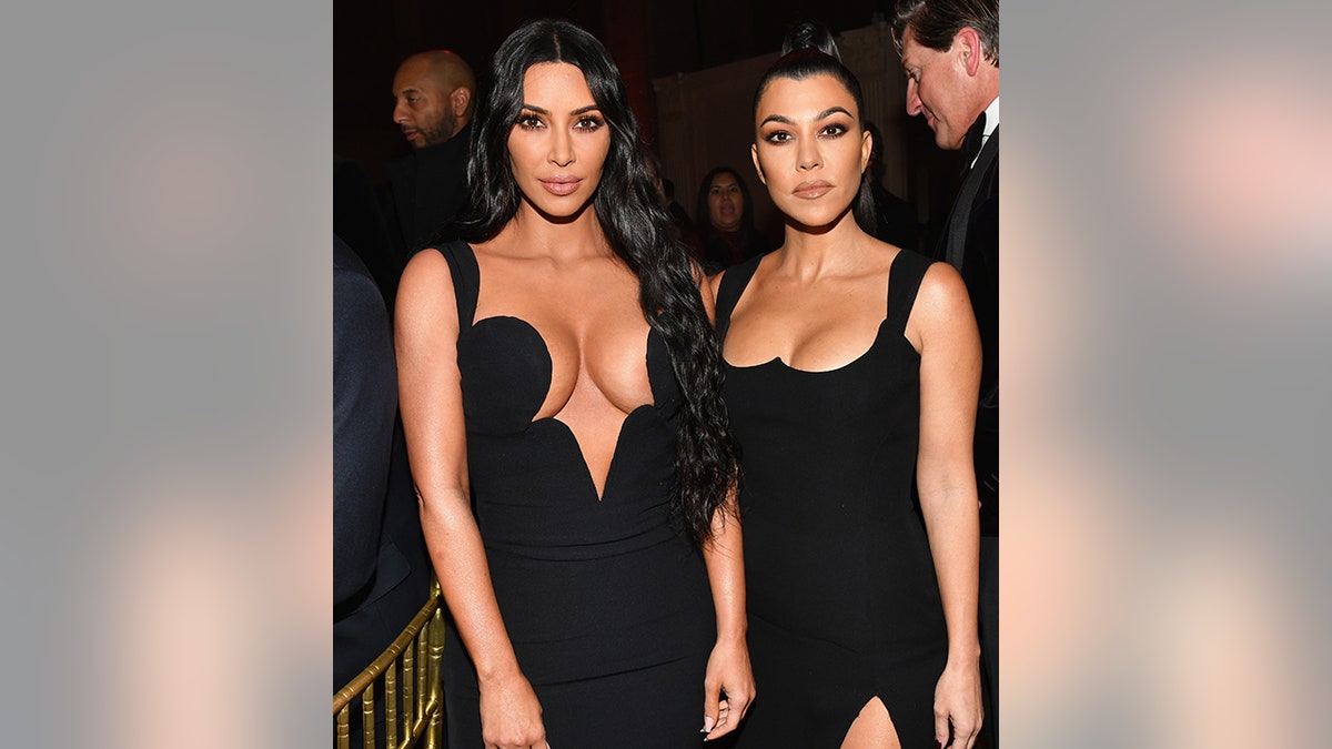 Kim Kardashian in a very plunging black gown poses for a photo with sister Kourtney Kardashian in a black dress at the amfAR Gala